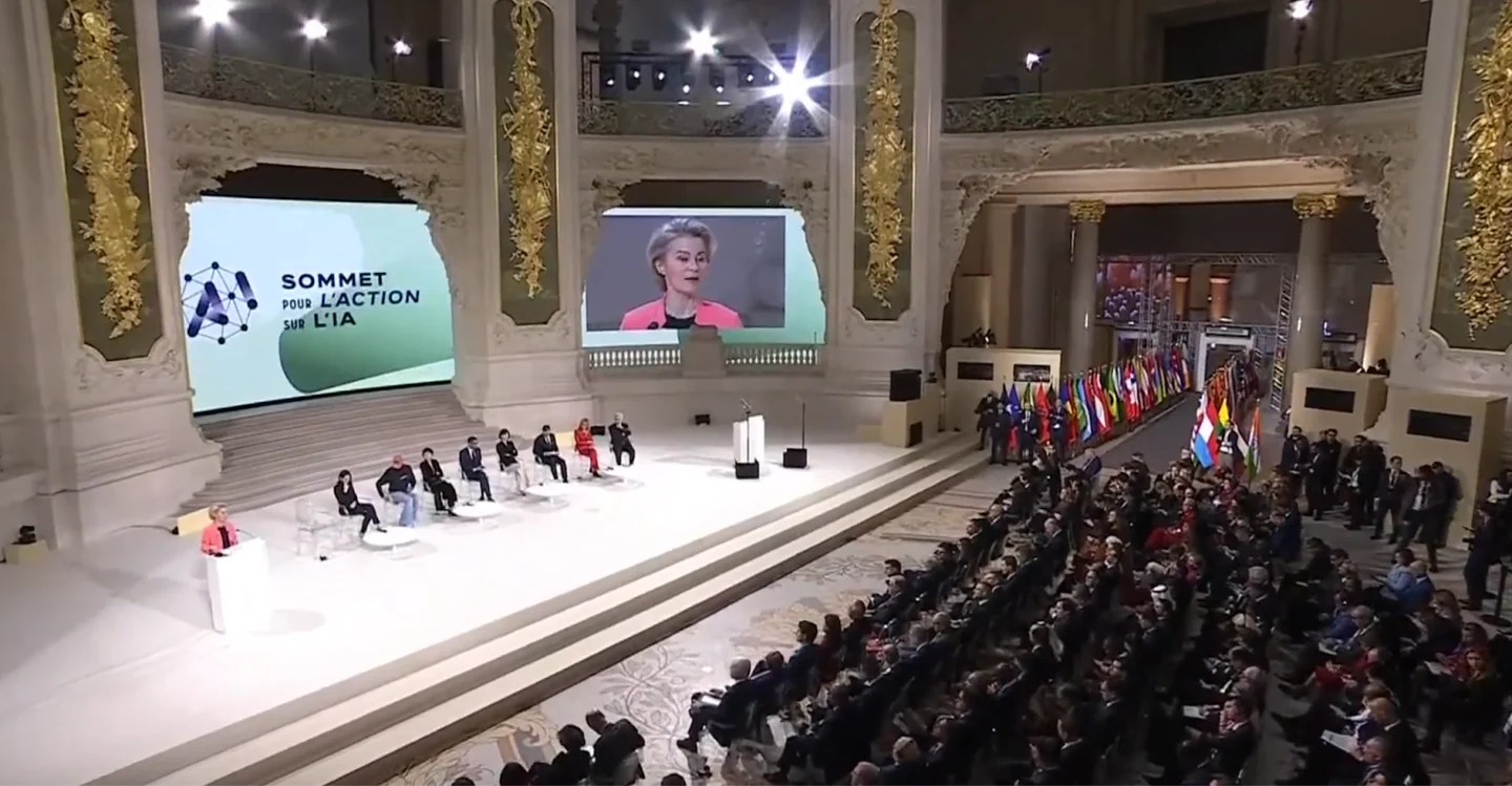 The Paris AI Action Summit hall, with a speaker at the lectern, panellists, an audience and national flags.
