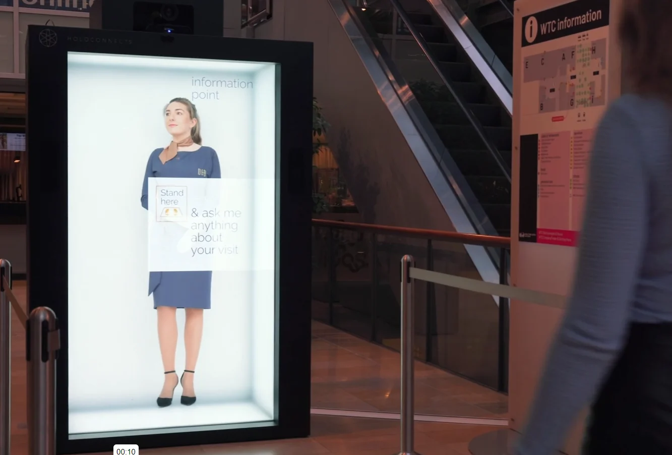 A Holoconnects booth displays a full-length virtual information assistant in a public building.