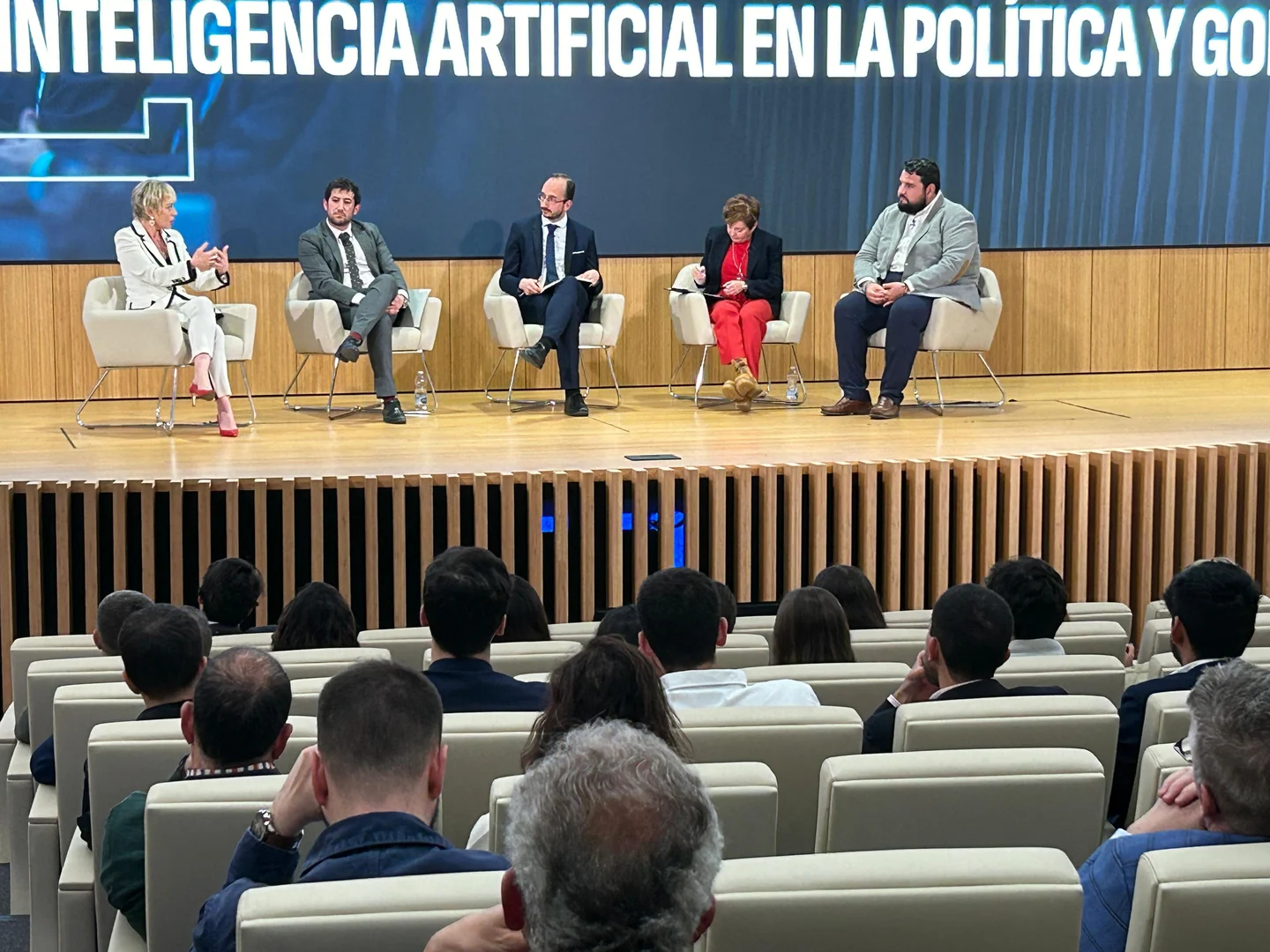 Five panellists seated on stage at estrategIA's event, with audience members in the foreground.